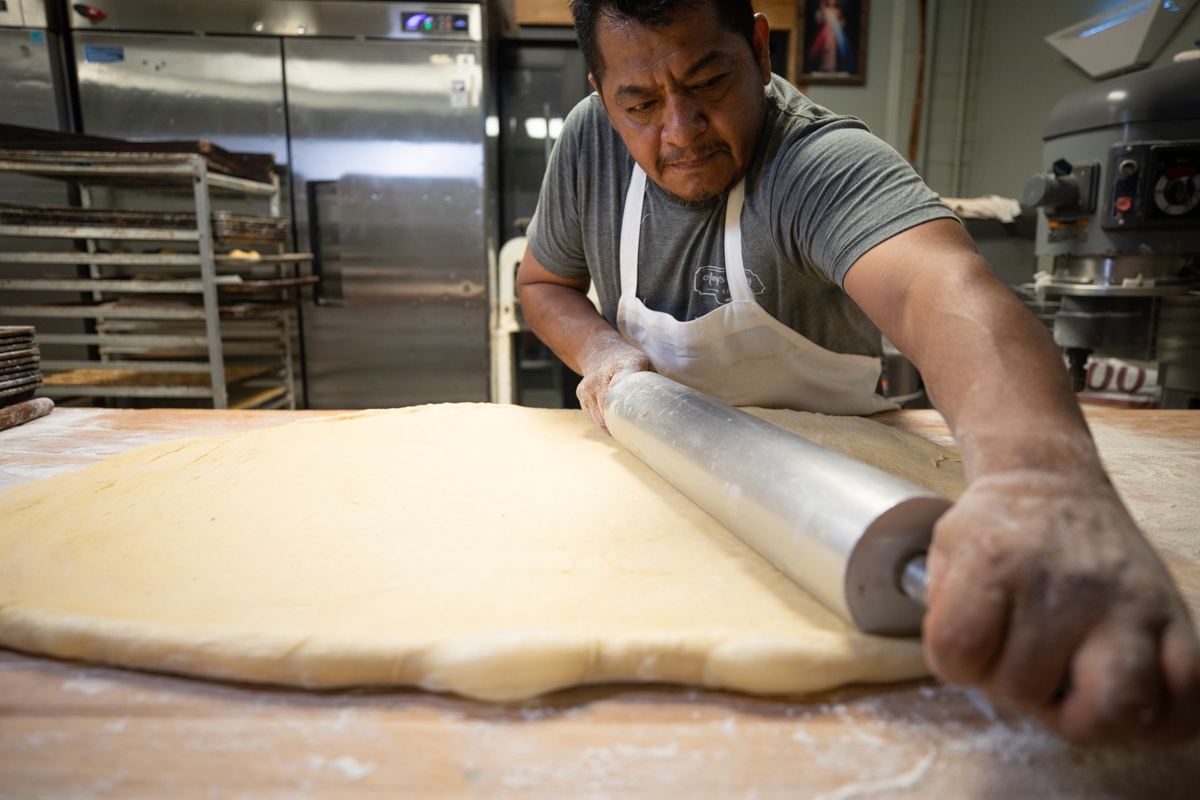 baker using rolling pin to flatten dough